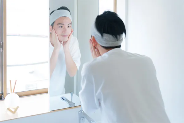 Młody mężczyzna po umyciu i osuszeniu skóry twarzy, wklepuje w skórę krem pielęgnacyjny